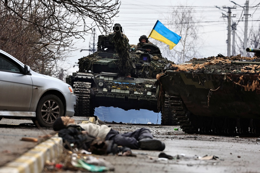 Ukrainische Armeesoldaten sitzen auf ihrem Panzer, während die Leiche eines Zivilisten, der laut Anwohnern von russischen Armeesoldaten getötet wurde, inmitten der russischen Invasion in der Ukraine auf der Straße liegt, in Bucha, Region Kiew, Ukraine, 2. April 2022.