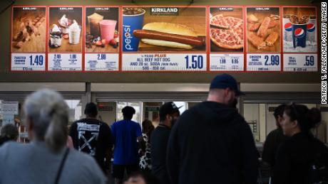 Kunden warten in der Schlange, um die unten stehenden Schilder für ein 1,50-Dollar-Set mit Hot Dog und Soda von Costco Kirkland zu bestellen.